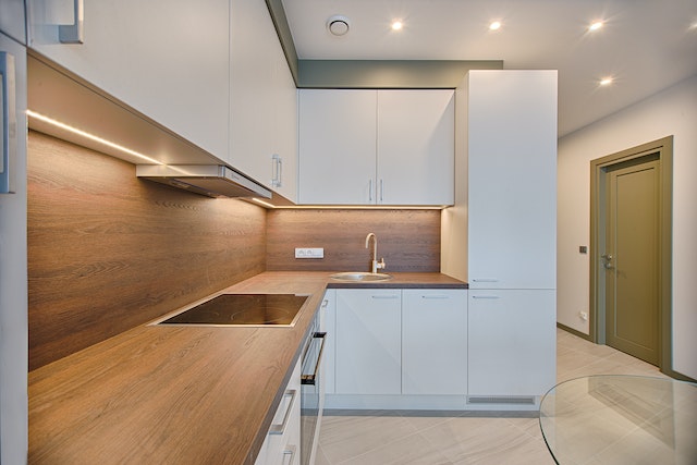 L-shaped apartment kitchen with lightwood counters and white cabinets